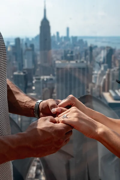 Close-up of a couple’s hands during a proposal at Top of the Rock, with a sparkling engagement ring and the New York skyline in the background. The perfect detail shot for capturing the emotion of a Rockefeller Center engagement.
