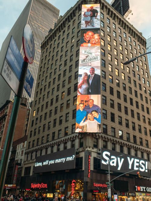 Tall building in Times Square with a vertical LED billboard of couple photos and a Say YES! sign at street level
