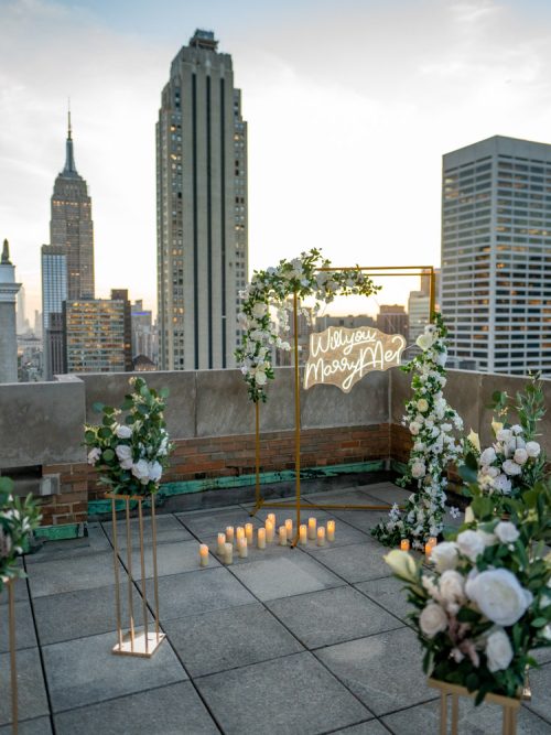 Terrace with white floral stands, a gold arch, candles and a neon sign, with the Empire State Building beyond