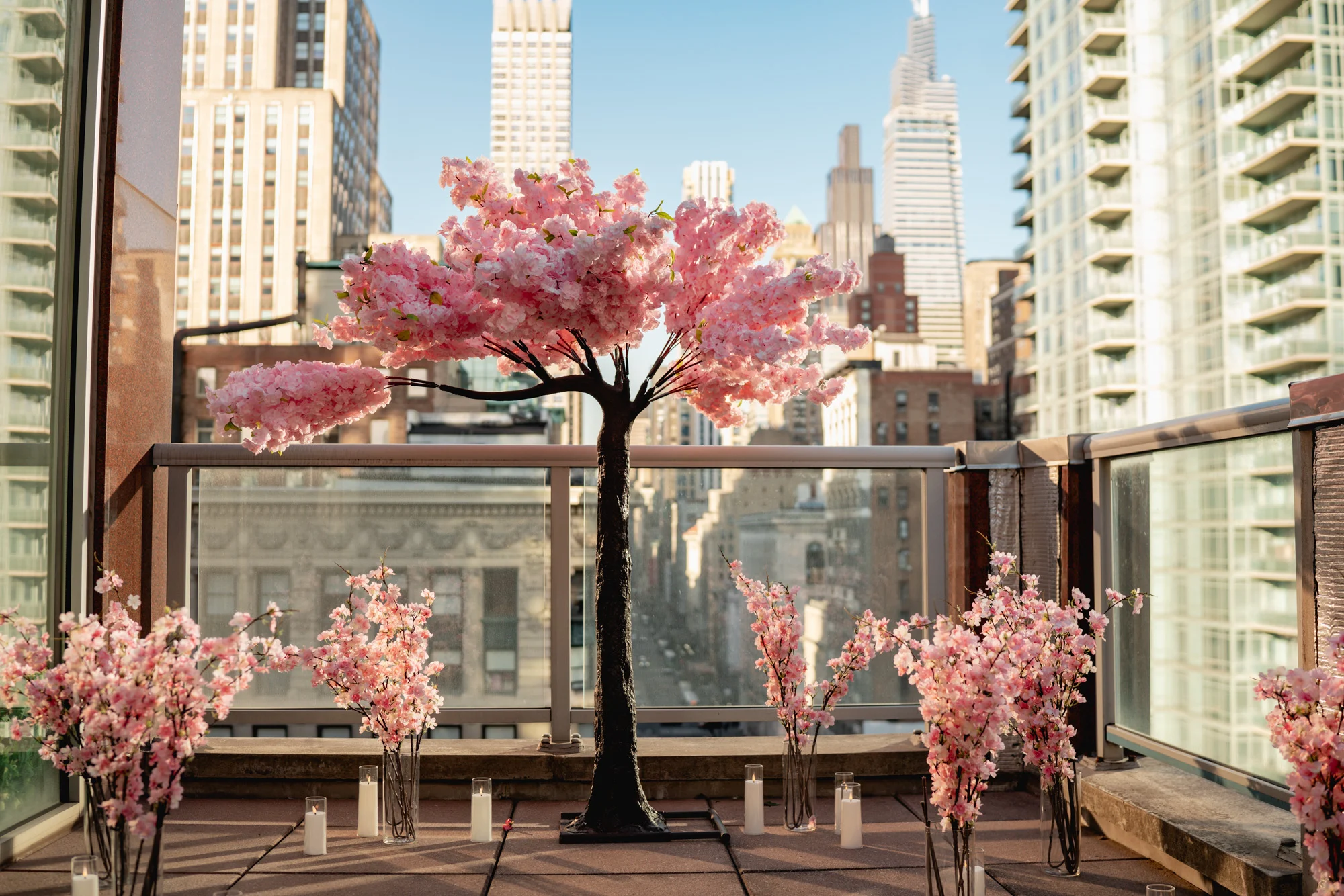 Pink cherry blossom tree and blossom vases with candles on a terrace with Midtown Manhattan towers behind