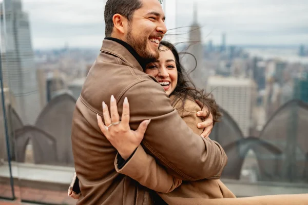 Newly engaged couple celebrating at Top of the Rock observation deck with panoramic views of New York City.