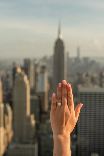 Close-up of engagement ring held up against the Empire State Building view from Top of the Rock, post-proposal photo.