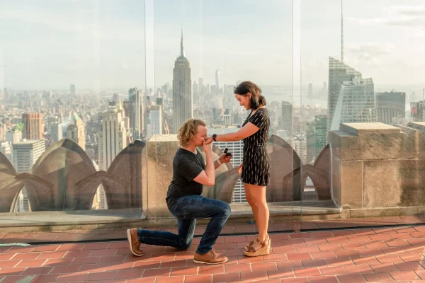 A romantic marriage proposal at Top of the Rock in Rockefeller Center, with the groom-to-be on one knee and the iconic Empire State Building towering in the background. This unforgettable NYC engagement moment captures the skyline at golden hour, making it one of the most picturesque proposal spots in New York City.