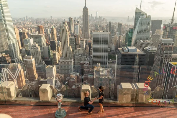 Surprise proposal at Top of the Rock with panoramic view of Manhattan and Empire State Building in the background, Rockefeller Center engagement.