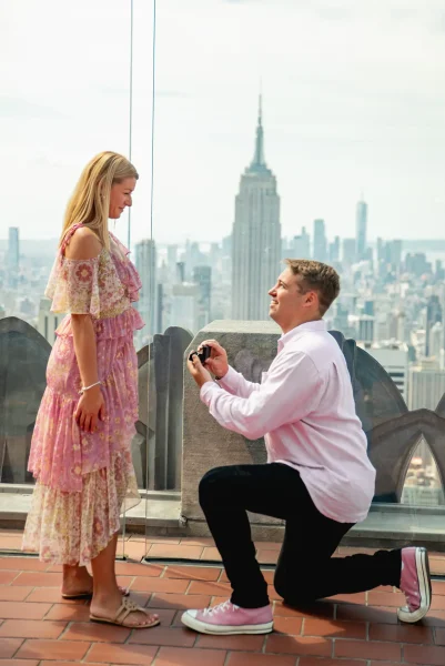 Man proposing to his partner at Top of the Rock with the NYC skyline and Empire State Building in the background, Rockefeller Center engagement.