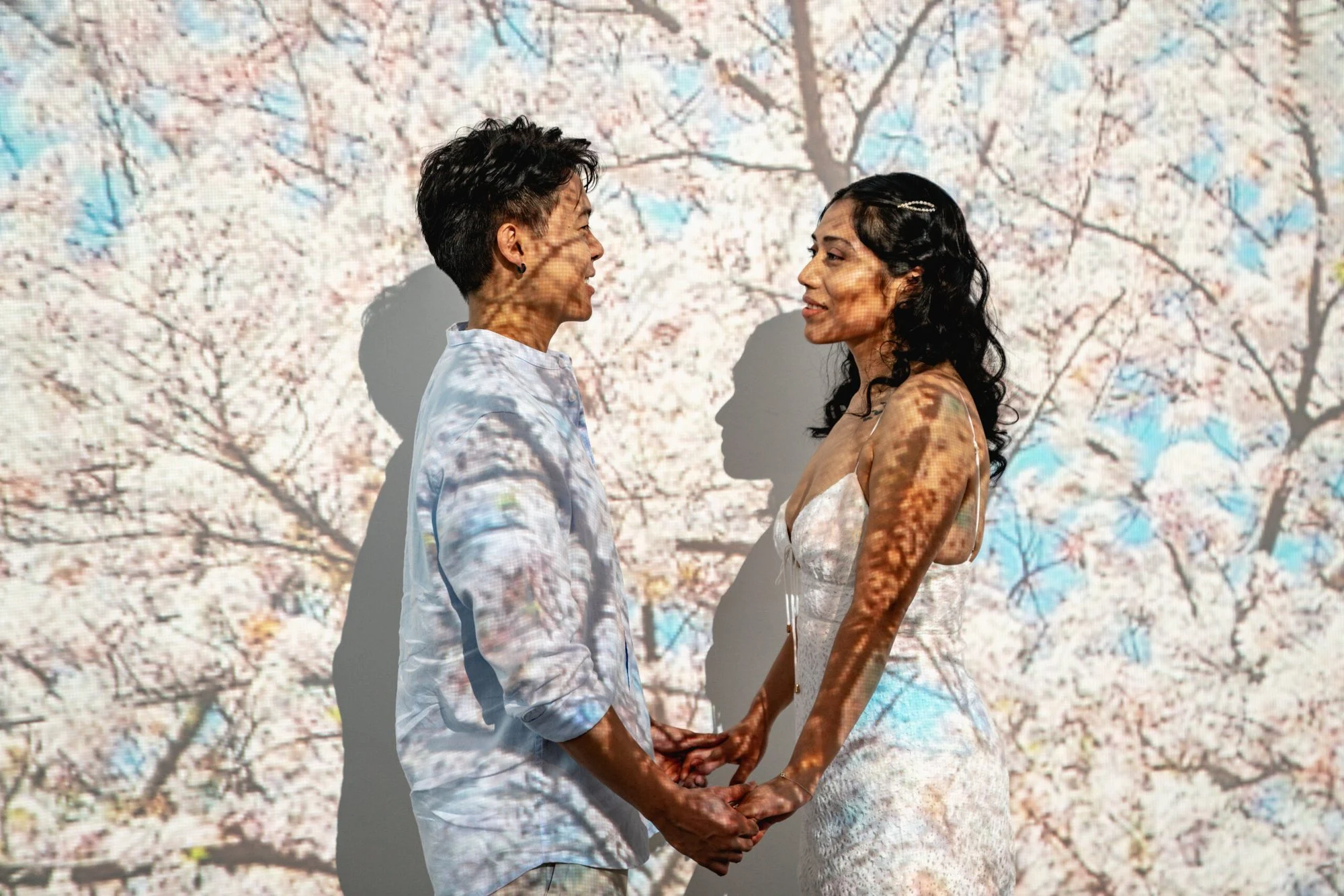 Couple holding hands as projected cherry blossom patterns and shadows fall across them and the wall