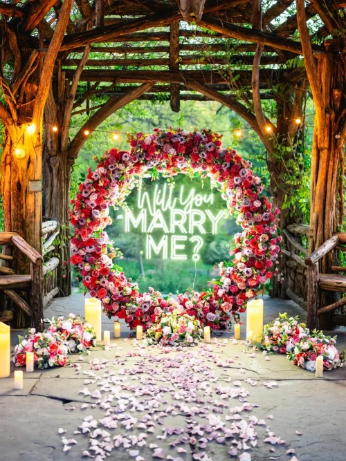 Round red rose arch with a Will You Marry Me neon sign, candles and a petal path inside a rustic Central Park gazebo