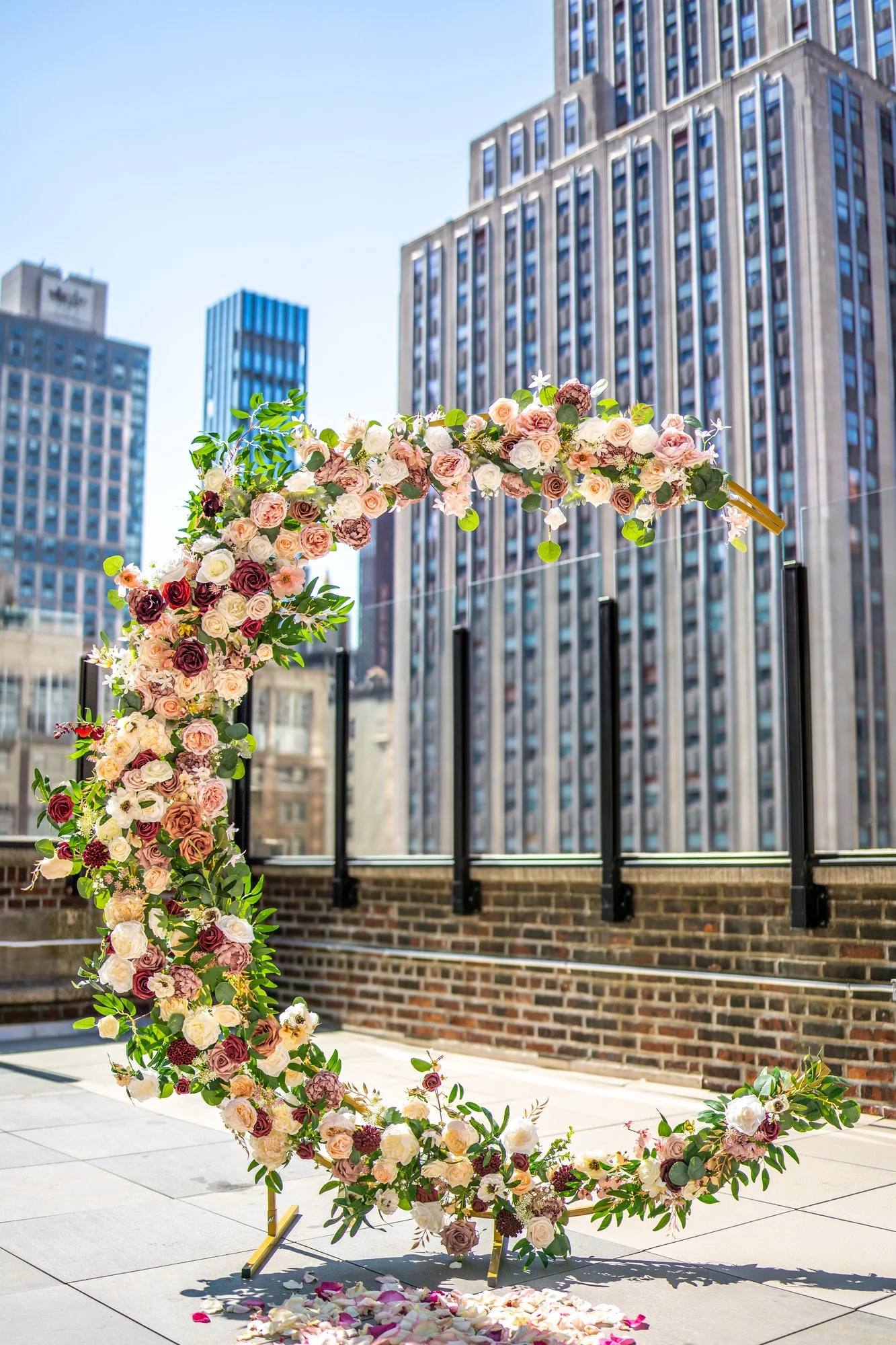 Crescent flower arch with pink and burgundy roses on a rooftop surrounded by Manhattan skyscrapers