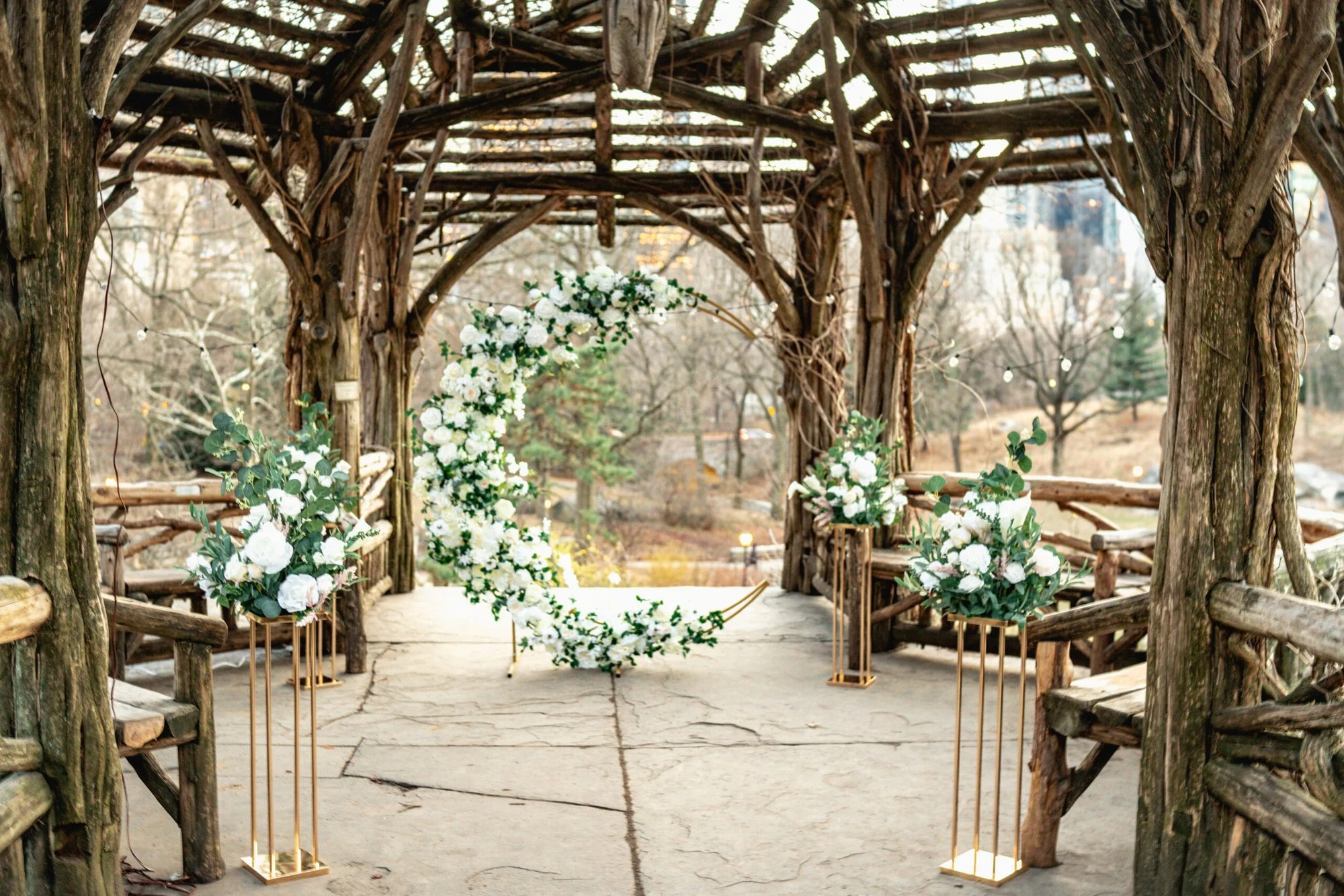 White crescent flower arch and floral stands inside a rustic Central Park gazebo